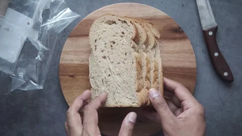 Hands placing sliced whole wheat bread onto wooden cutting board for prepar.. Stock Footage 332744889