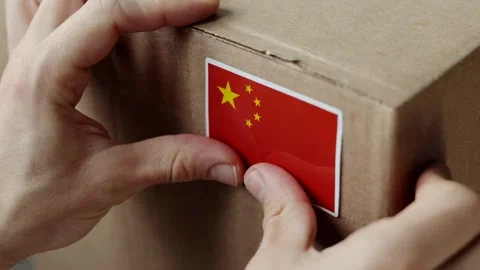 Hands placing a sticker of the Chinese flag on a cardboard shipping box. Stock Footage 323469382