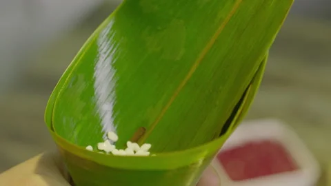 Hands Placing Sticky Rice and Dates into Folded Banana Leaf Cone 库存影片 335501546