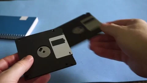 Hands placing two old 3.5 inch floppy disks for data storage on a blue desk Stock Footage 340118444