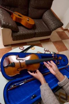 Hands placing a violin in its case with a guitar in the background Stock Photos