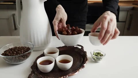 Hands placing a white bowl of dates beside small finjan cups on copper tray.. Video stock 332791558