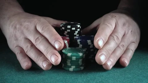 Hands of a player carefully arranging colorful poker chips on a green felt Stock Footage 338412238