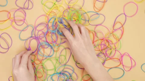 Hands playing with bunch of colorful rubber bands on yellow background Stock Footage 232351153