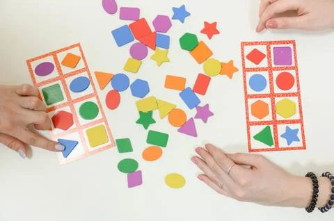 Hands playing shape matching game with colorful geometric pieces on table Foto stock