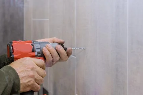 Hands of plumber using a drill to create new holes in tile bathroom Stock-Fotos