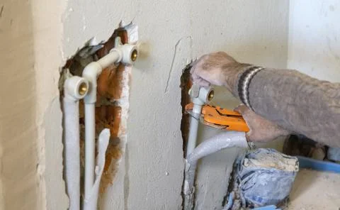 Hands of plumbers in gloves cut a plastic pipe with a pipe cutter. Installation Photos