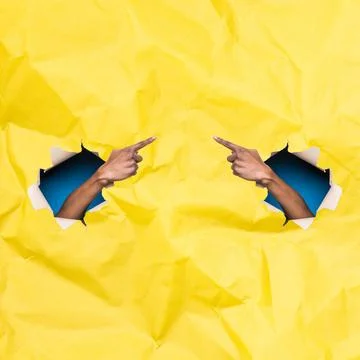 Hands Pointing at Each Other Through Torn Holes in Yellow Paper against Blue Bac Stock Photos