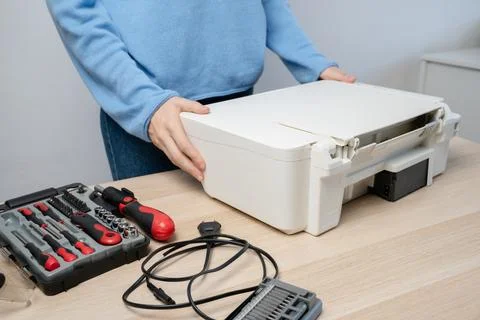 Hands position a white all-in-one printer on a desk with a toolkit and power  Stock Photos