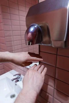 Hands Positioned Under Modern Hand Dryer in a Stylish Restroom with Pink Tiles Stock Photos