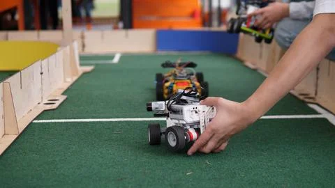 Hands positioning small wheeled robot on indoor racing track during engineering Stock Photos