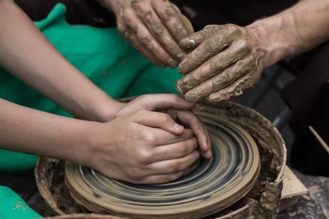 Hands of a potter, helping to a boy create an earthen jar on the circle Stock Photos