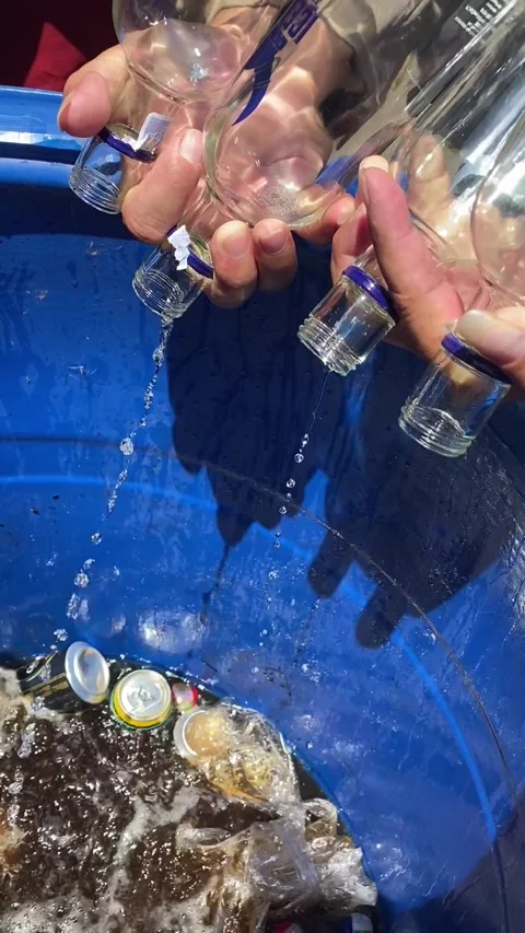 Hands Pouring Seized Illegal Hard Liquor from Bottles into a Barrel Stock Footage 321536876