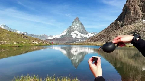 Hands pouring tea from a teapot into a mug with the iconic Matterhorn mountain i Stock Footage 312637091