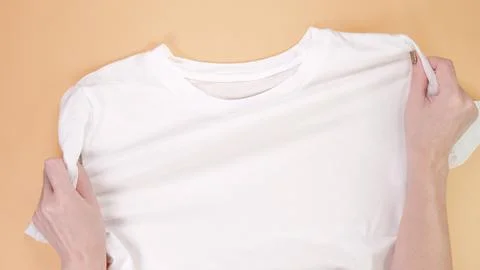 Hands Preparing a Clean White T-Shirt on Beige Background, Ready for Custom Stock Photos