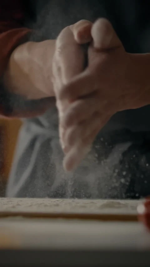 Hands preparing dough with flour on a wooden countertop in a cozy kitchen en Stock Footage 331597691