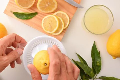 Hands preparing a lemonade squeezing a lemon on bench top Stock Photos