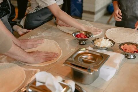 Hands preparing pizza dough with fresh ingredients in kitchen cooking class Stock Photos