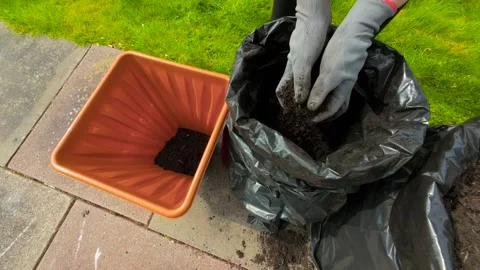 Hands preparing planter for flowers, scooping soil from black garden bag. Female Stock Footage 309020024