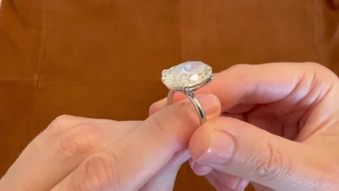 Hands presenting oval diamond platinum ring with suede backdrop Video stock 316747859