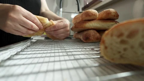 Hands pressing torn bread onto wire cooling rack beside stack of freshly baked Stock Footage 339306727
