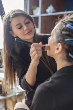 Hands of professional makeup artist applying eyeshadow concealer on eyes of Stock Photos