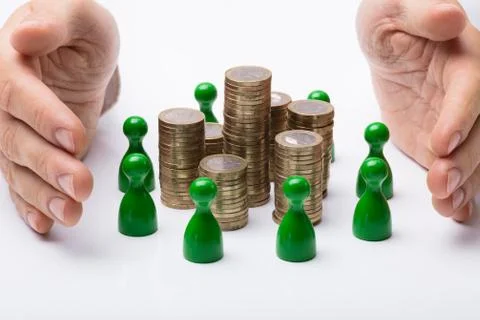 Hands Protecting Coin Stack Surrounded With Green Figures Stock Photos