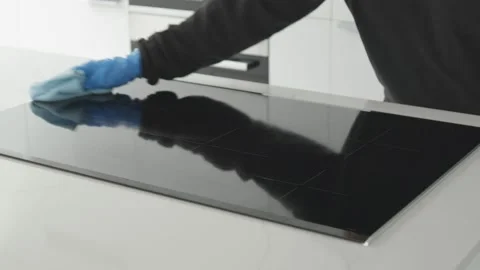 Hands in protective glove cleaning a modern electric stove with rag Stock Footage 158577236