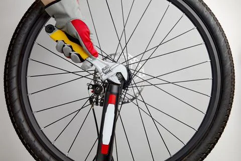 Hands in protective gloves with an adjustable wrench unscrew the bicycle wheel Stock Photos