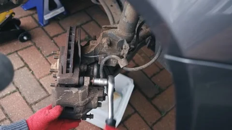 Hands in protective gloves removing brake caliper slider bolt during vehicle Stock Footage 345714797