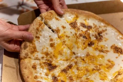 Hands pulling apart slices of cheese pizza in a takeout box at home Stock Photos