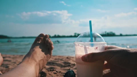 Hands Put a Milkshake on the Background of Women's Legs and the Beach Stock Footage 200944865