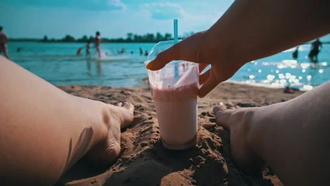 Hands Put a Milkshake on the Background of Women's Legs and the Beach Stock Footage 200975302