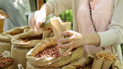 Hands put nuts into bag. Nuts on the counter. Video stock 85975746