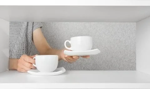 Hands put on the shelf cups with saucers Stock Photos