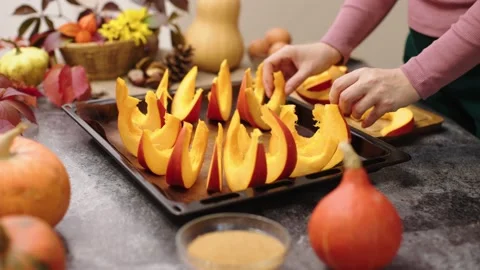 Hands put sliced orange pumpkin pieces on baking pan prepare baked in oven Video stock 218793407