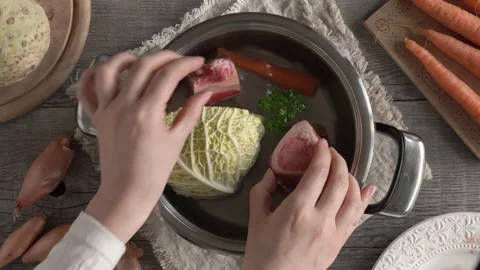 Hands putting beef marrow bones and meat into a pot with water and vegetables Video stock 171991413