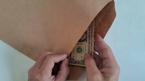 Hands putting cash into a paper envelope. Person inserting dollar bills for Stock Footage 340360130