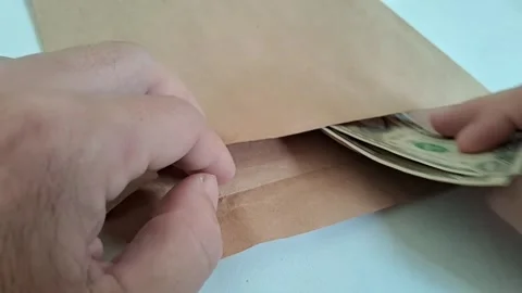 Hands putting cash into a paper envelope. Person inserting dollar bills into a Stock Footage 340360131