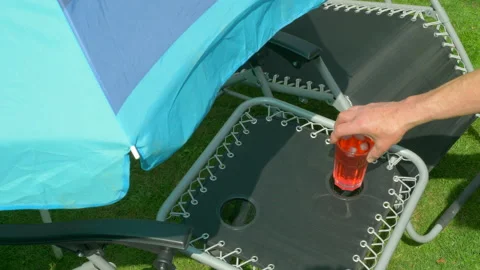 Hands putting fruit drink with ice in small outside table next to sun lounger. Video stock 135593377