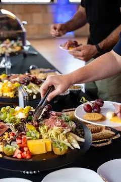 Hands reaching for appetizers on a catering table at a social event Stock Photos