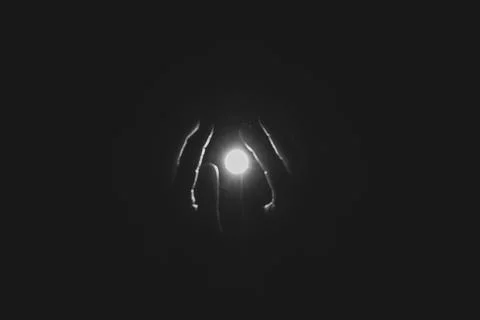 Hands reaching for a bright light bulb in complete darkness for themes of p.. Stock Photos