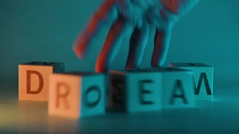 Hands rearrange blocks with letters to form the word dream in a colorful and Stock-Footage 338187720