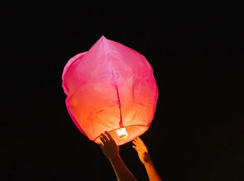 Hands release a paper flashlight into the night sky. Inside the lantern, the  Stock Photos
