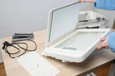 Hands remove the flatbed scanner lid from a multifunction printer on a wooden Stock Photos