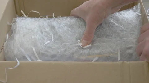 Hands removing bubble wrapped package from box with shredded paper packaging. Video stock 143097073