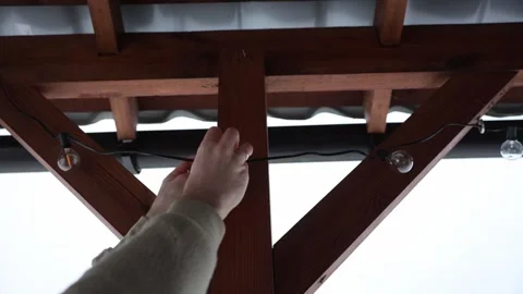 Hands Replacing LED String Light Bulbs on Wooden Terrace Structure Stock Footage 297635766