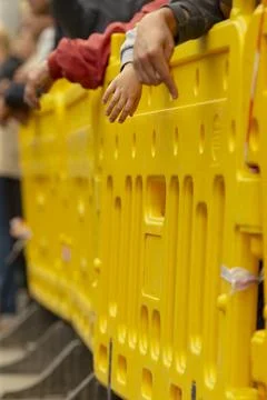 Hands resting on bright yellow crowd control barrier at public event Stock Photos