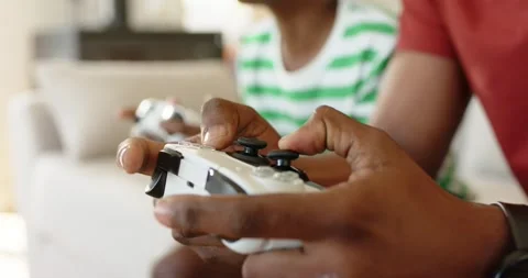 Hands resting on controllers pressing triggers, friends leaning in gameplay on Stock Footage 341664890