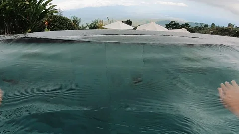Hands resting on pool edge above tropical infinity pool with rippling water Stock Footage 338444096
